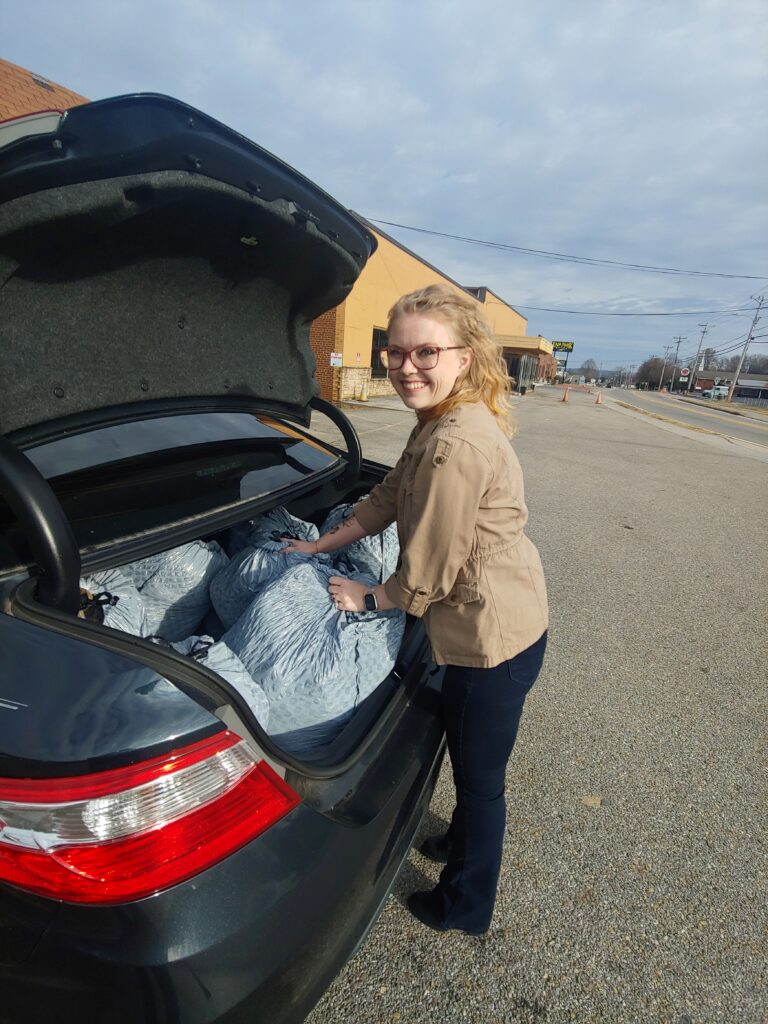 A white woman loads large plastic bags into the trunk of a car