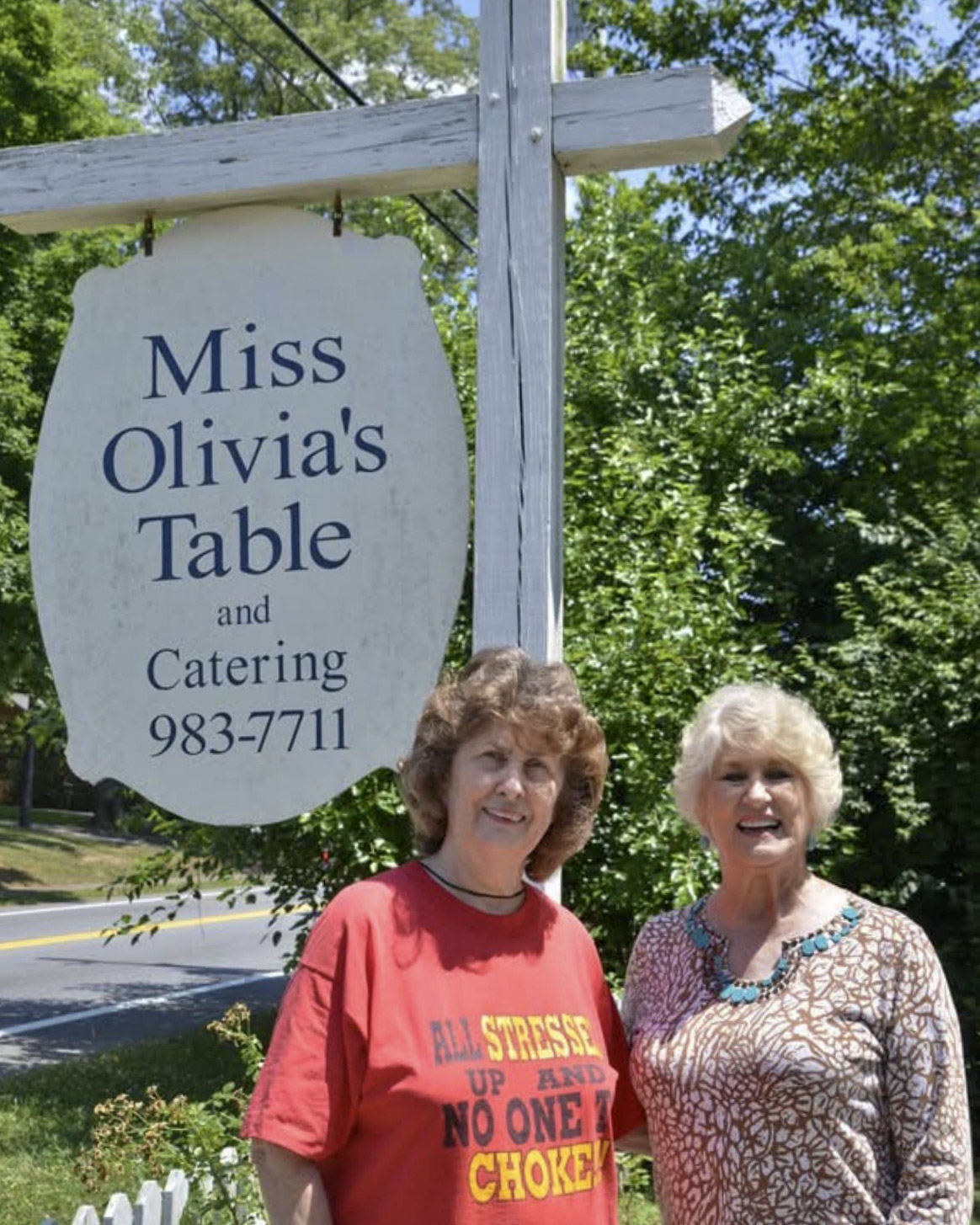 Olivia Sipe stands with a former customer in front of the iconic Miss Olivia's Table sign.